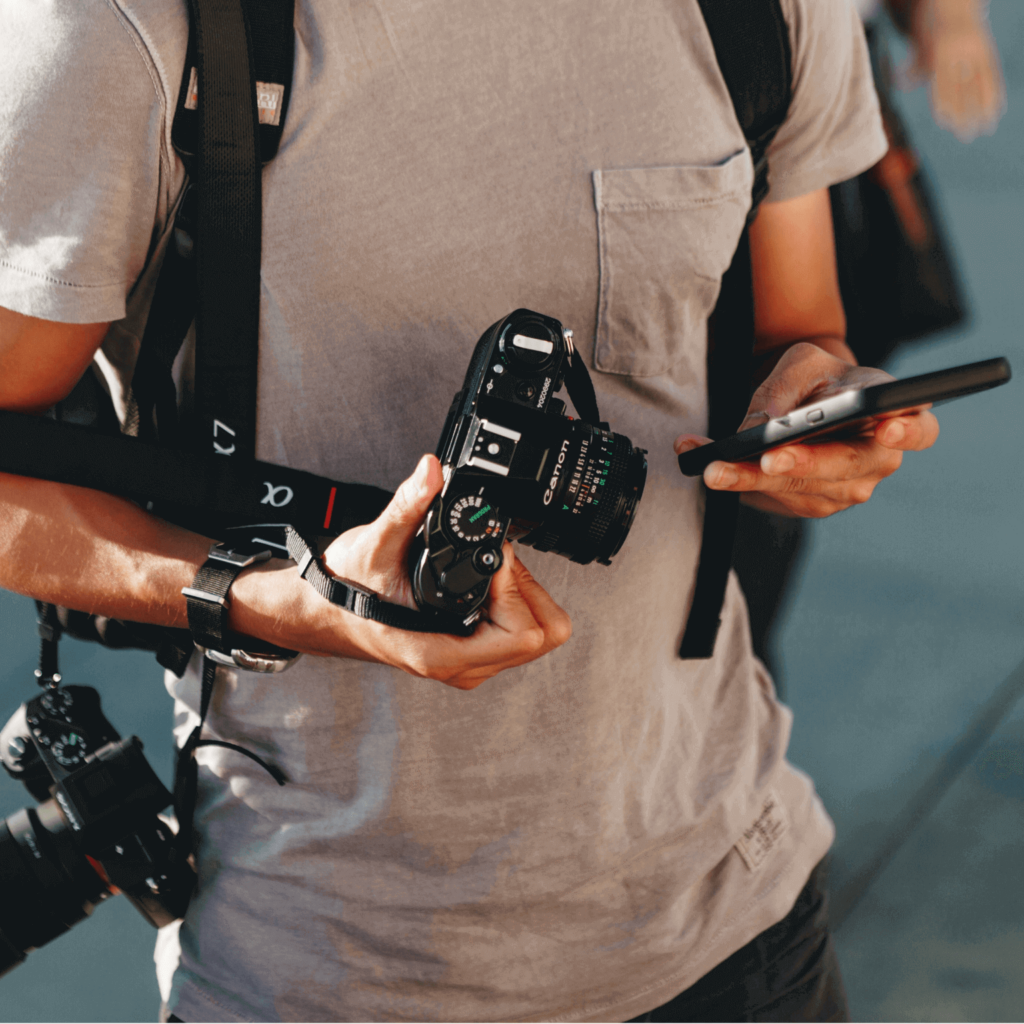 Person holding a phone and a camera, with another camera slung over their shoulder.